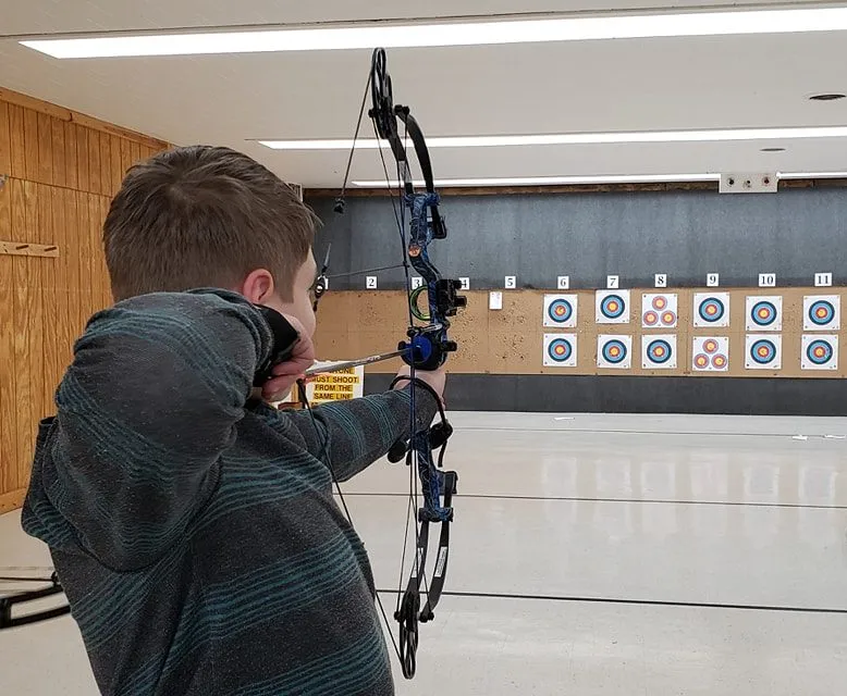 over the shoulder view of a young archer aiming at paper targets on an indoor range