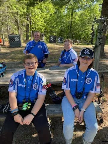 four youth archers in their matching team jerseys outside at a picnic table taking a break during competition
